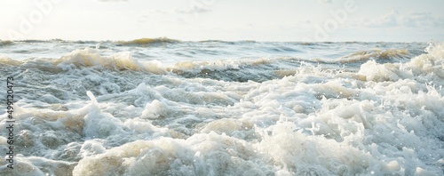 Baltic sea shore after the storm. Sunset, soft golden sunlight. Water surface texture, crashing waves and splashes, foam. Picturesque panoramic scenery. Idyllic seascape. Nature, environment, ecology