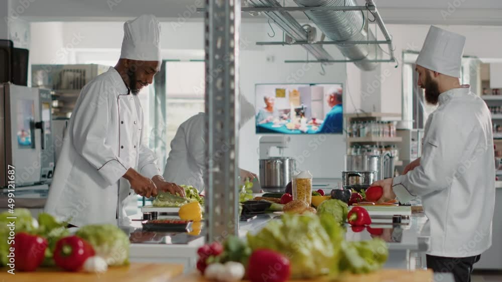 Diverse team of chefs making meal preparations with ingredients, cooking delicious gourmet dish in restaurant kitchen. People in uniform working as cooks preparing gastronomy food recipe. Diverse team of chefs making meal preparations with ingredients, cooking delicious gourmet dish in restaurant kitchen. People in uniform working as cooks preparing gastronomy food recipe.