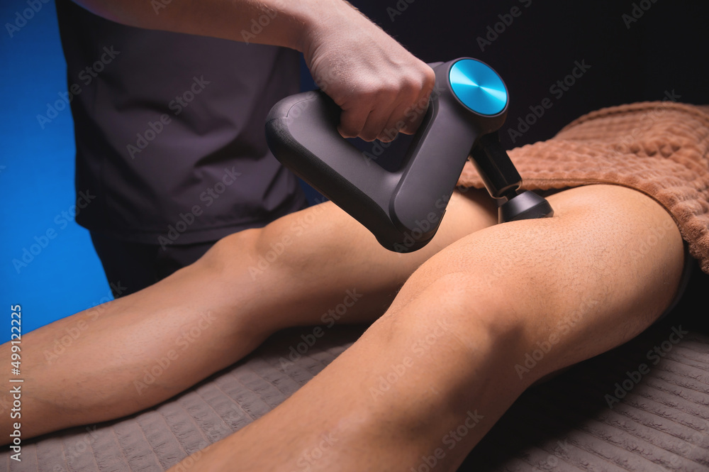 Fototapeta premium Percussion massage on the back of the leg. Massage the back of the thigh and the back of the calf muscles. Working as a percussion massager