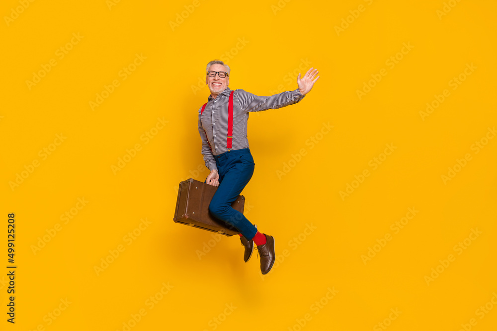 Full body photo of flying pensioner enjoy traveling with retro valise say you hello isolated on yellow color background