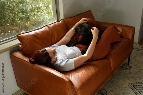 full length portrait o red haired girl wearing casual clothes, relaxing on comfortable leather couch in living room home setting.