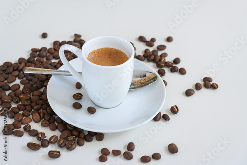 Espresso in a small coffee cup, spoon and roasted beans on a white table, copy space, selected focus