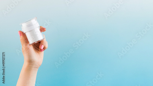 A mock-up of a jar of moisturizer in a woman's hand on a blue background. Copy space. 