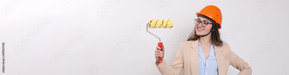Girl engineer in an orange construction helmet with plastering painting tools in her hands on a white background. Girl engineer in an orange construction helmet with plastering painting tools in her hands on a white background.