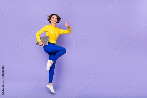 Fototapeta Naklejka Na Ścianę i Meble -  Full size photo of cool millennial brunette lady jump thumb up with laptop wear shirt trousers shoes isolated on purple background
