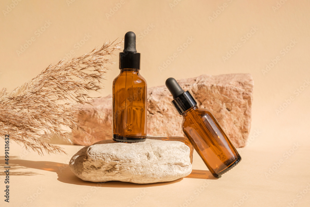 Naklejka premium Dark amber glass bottle standing on stone. Natural skin care SPA beauty product design. Mineral organic oil cosmetics on beige background. Mock-Up. Oily pipette. Face and body treatment. Front view