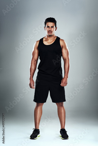 It comes with the lifestyle. Full length portrait of a sporty young man standing against a grey background.