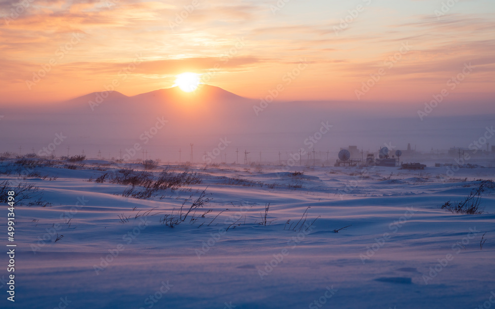 Satellite dishes in the winter snow-covered tundra in the Arctic. Sunset over the tundra and mountains. Cold frosty winter weather. Winter arctic landscape. Chukotka, Siberia, Far North of Russia.