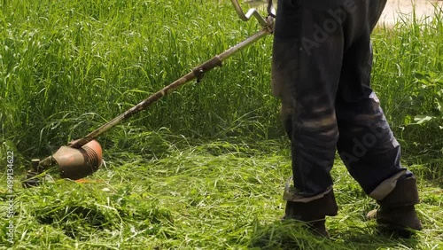 The garden mower cuts the grass of the trimmer.The guy uses a hand-held grass trimmer to green his garden on a sunny spring day. Unrecognizable man uses petrol scythe to cut grass
