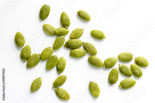 Raw peeled pumpkin seeds scattered on a white background, top view