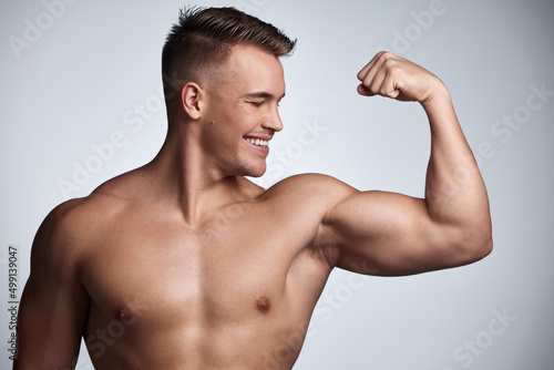 Pump some iron. Studio shot of a muscular young man flexing his arm against a grey background.