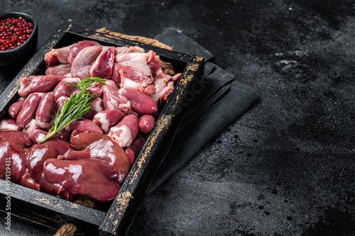 Uncooked Bird offals, raw chicken giblets, gizzards, stomachs, liver and hearts in a wooden tray. Black background. Top view. Copy space