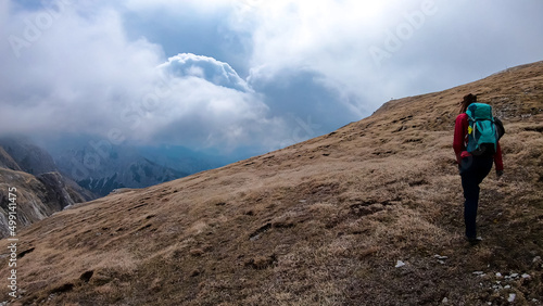 Woman with backpack on scenic hiking trail with view on cloud covered mountain peaks of the Hochschwab Region in Upper Styria, Austria. Dry alpine meadows in beautiful Alps, Europe. Freedom vibe. Rain