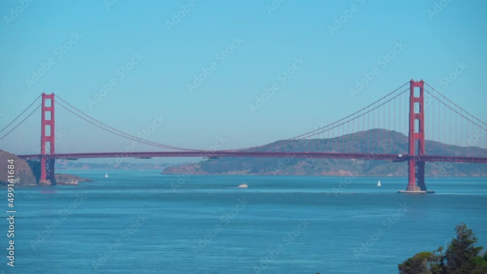 Wide shot: Famous Golden Gate Bridge during sunny day with cruising boats on river Wide shot: Famous Golden Gate Bridge during sunny day with cruising boats on river