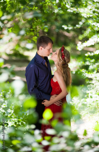 Young beautiful lovers guy and girl in a red dress are hugging in the summer in a green forest