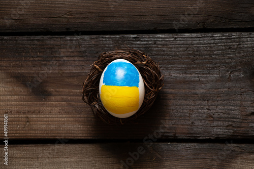 One white chicken egg with a painted flag of Ukraine in a straw basket on the table at home, culture and holidays