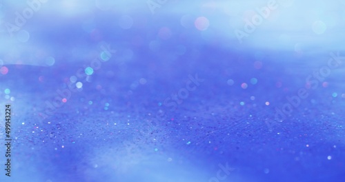 Glitter abstract background. Bokeh light. Glitz gleam. Defocused neon colorful sparkling circles on blue white grain texture overlay.