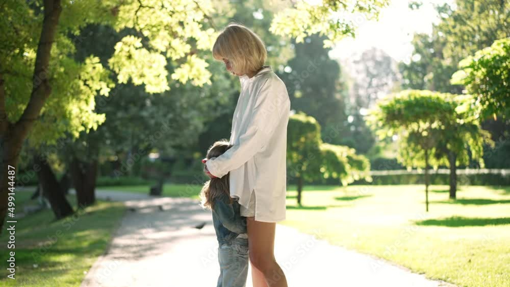 Young Caucasian mother hugging little daughter in sunbeam in spring summer park. Portrait of confident happy woman talking with girl in slow motion enjoying weekend on sunny day Young Caucasian mother hugging little daughter in sunbeam in spring summer park. Portrait of confident happy woman talking with girl in slow motion enjoying weekend on sunny day