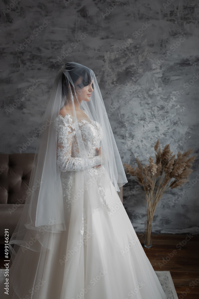 Portrait of the bride. Attractive young girl look at the camera in a white wedding dress and veil holding a bouquet of white and pink flowers in her hands on a background of green trees Portrait of the bride. Attractive young girl look at the camera in a white wedding dress and veil holding a bouquet of white and pink flowers in her hands on a background of green trees