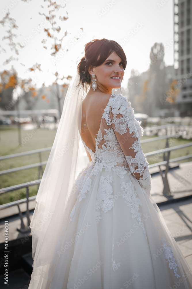 Portrait of the bride. Attractive young girl look at the camera in a white wedding dress and veil holding a bouquet of white and pink flowers in her hands on a background of green trees Portrait of the bride. Attractive young girl look at the camera in a white wedding dress and veil holding a bouquet of white and pink flowers in her hands on a background of green trees