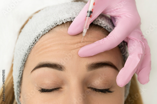 Close-up of the hands of an expert cosmetologist injecting botox into a woman's forehead. Correction of forehead and eye wrinkles with botulinum toxin