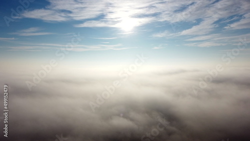 Aerial drone view flight over fog and under clouds with shining sun shining. Fly through clouds. Amazing beautiful nature landscape. Scenic aerial view moving white clouds in blue sky. Seamless loop.