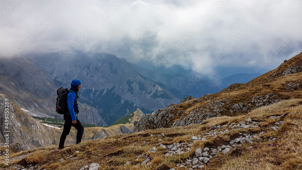 Man with backpack on scenic hiking trail with view on cloud covered mountain peaks of the Hochschwab Region in Upper Styria, Austria. Dry alpine meadows in beautiful Alps in Europe. Freedom vibe. Rain