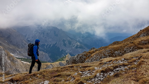Man with backpack on scenic hiking trail with view on cloud covered mountain peaks of the Hochschwab Region in Upper Styria, Austria. Dry alpine meadows in beautiful Alps in Europe. Freedom vibe. Rain © Chris