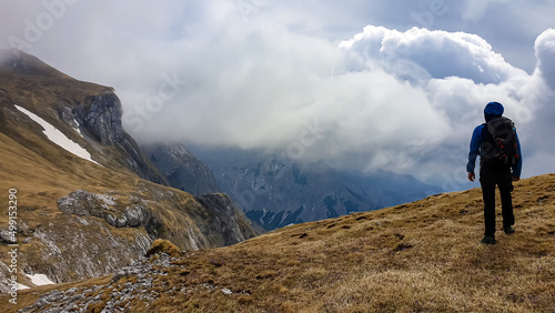 Man with backpack on scenic hiking trail with view on cloud covered mountain peaks of the Hochschwab Region in Upper Styria, Austria. Dry alpine meadows in beautiful Alps in Europe. Freedom vibe. Rain