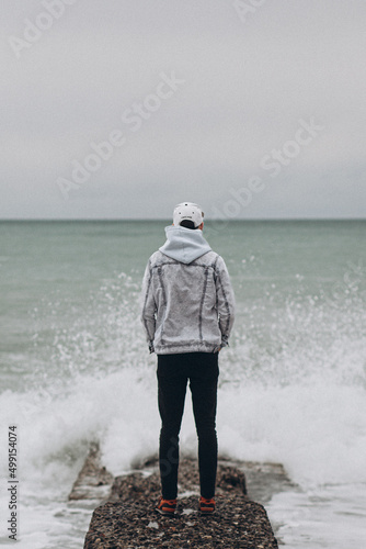 Man with hat standing back on the sea at wave splash cloudy weather sea stone (ID: 499154074)