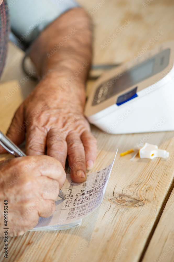 Mano de cerca y hombre mayor escribiendo resultados de las mediciones de la tensión Mano de cerca y hombre mayor escribiendo resultados de las mediciones de la tensión