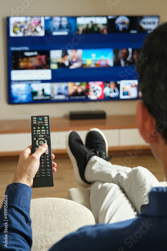 man sitting on the sofa with his legs stretched out looking for content to watch on tv photo
