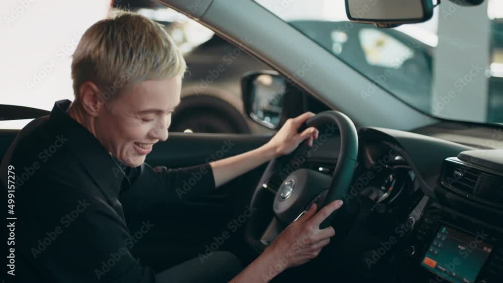 Stylish girl sitting in the car evaluates the interior of the car inside. The woman is happy, smiling and rejoicing in the purchase new car. Girl in awe of new vehicle. The buyer selects a car. Stylish girl sitting in the car evaluates the interior of the car inside. The woman is happy, smiling and rejoicing in the purchase new car. Girl in awe of new vehicle. The buyer selects a car.