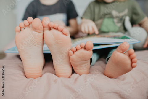 Big brother and little sister holding bare feet close up to camera . Blurred face on background 