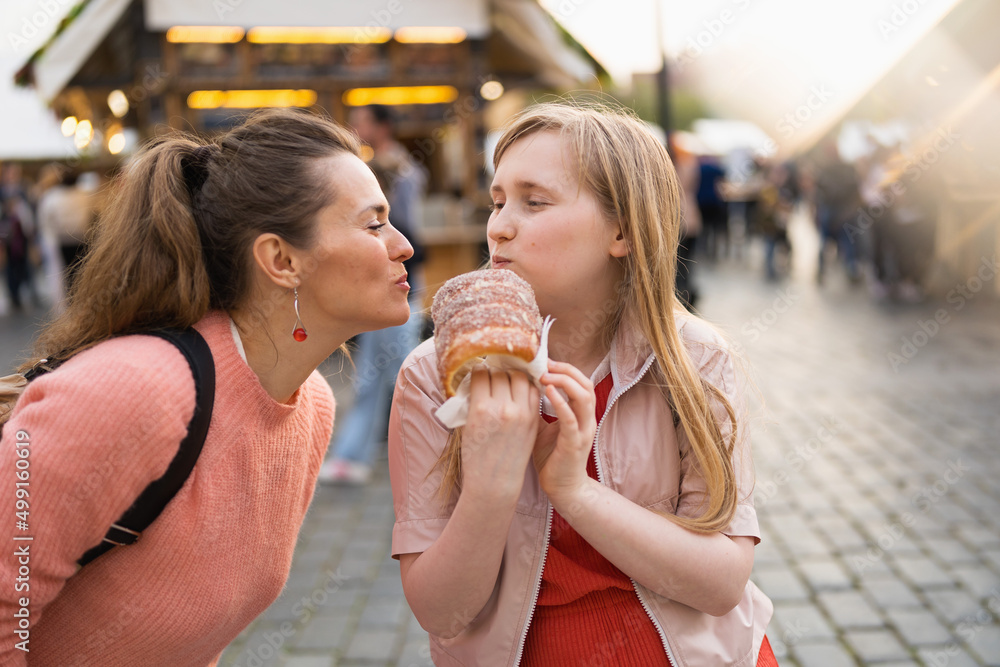 smiling mother and daughter at fair in city eating trdelnik smiling mother and daughter at fair in city eating trdelnik