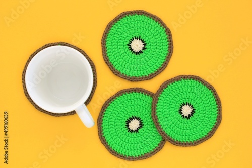 Kiwi fruit colurful crochet coasters and whie cup on yellow background. Home decor idea. DIY handmade kitchen accessories on a table. Summer bright concept. photo