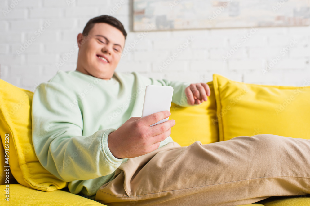 Smartphone in hand of blurred teenager with down syndrome on couch. Smartphone in hand of blurred teenager with down syndrome on couch.