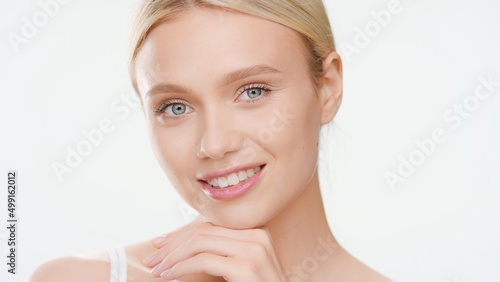 Big close-up beauty portrait of young white-skinned woman who touches her chin and smiles wide for camera on white background | Moisturizer commercial concept