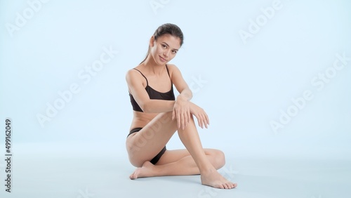 Young slim brunette Asian woman in black underwear sits on the floor and looks at the camera laying her hands on the knee on pale blue background   Body care and smooth legs concept © pavel_dp