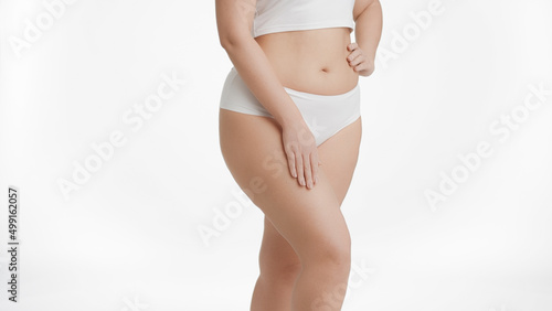 Medium shot of white-skinned plus size woman in white underwear strokes her thigh on white background | Unwanted leg hair removal concept