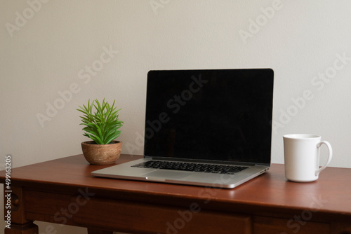 Mockup template for laptop, with a pot of plant and a white ceramic cup on a wooden table © Samuel