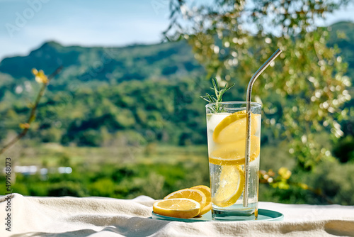 Foto Summer refreshing lemonade drink or alcoholic cocktail with ice, rosemary and lemon slices on the table in the garden