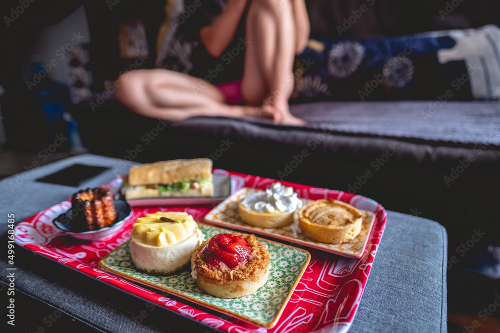 Delicious home breakfast with sexy girl (with red tray with colorful plates with apple pie, lemon pie, strawberries 'kuchen' cake, passion fruit cheese cake, gourmet sandwich and vanilla cake)