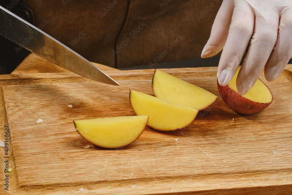 Slicing potatoes on a wooden chopping board. Cooking food. Sliced potatoes. Shallow depth of field Slicing potatoes on a wooden chopping board. Cooking food. Sliced potatoes. Shallow depth of field