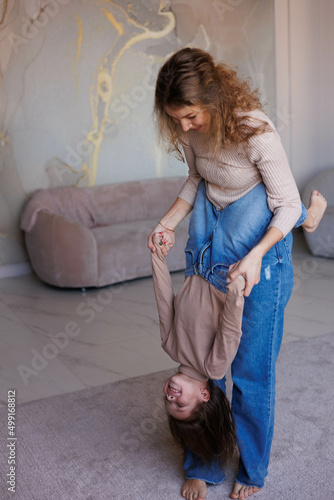 Lovely family mother and daughter embracing and kissing each other indoors. Happy sweet woman with little 6-year-old girl in casual clothers: turtlenecks and jeans. Mother holding daughter on hands photo