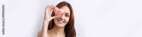 Beautiful smiling woman with clean skin, natural make-up and white teeth on a gray background. Holding a pink hygienic heart.