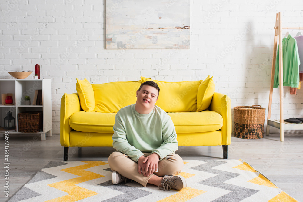Fototapeta premium Positive teenager with down syndrome sitting on floor at home.