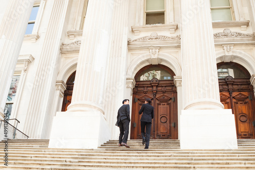 A well dressed man and woman look at each other as they walk up steps of a legal or municipal building in discussion. Could be business or legal professionals or lawyer and client.