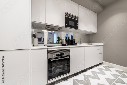 kitchen with white stone countertops, white cabinets, stainless steel appliances and integrated extractor hood, mirrored wall and stoneware floors