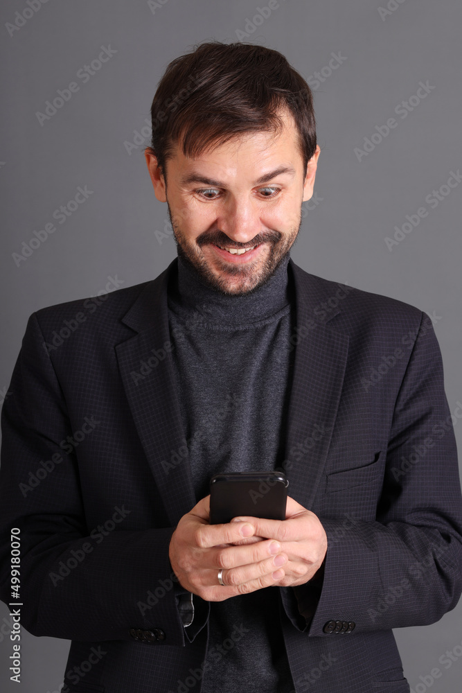 A smiling man in a jacket holds a cell phone in his hands A smiling man in a jacket holds a cell phone in his hands